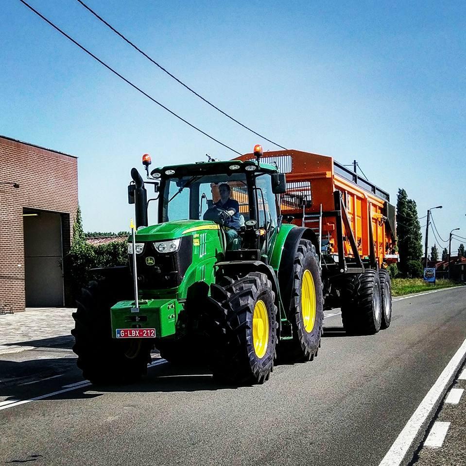 John Deere 6R-tractor met oranje kipwagen rijdt over een landelijke weg